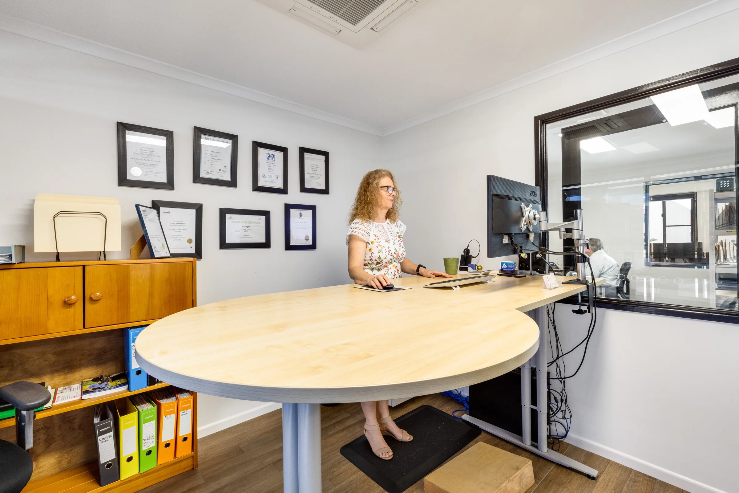 A Ready Accounting team member at a standing desk beside the practice's framed qualifications